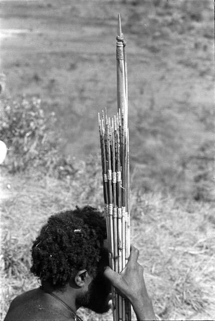 Man watching the battle from the end of the Waraara; his bundle of arrows and bow held in his right hand against his head