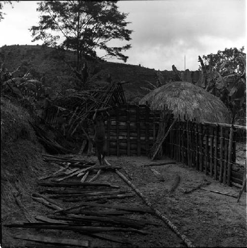 a woman carries old lumber from the old hunu to the new hunu