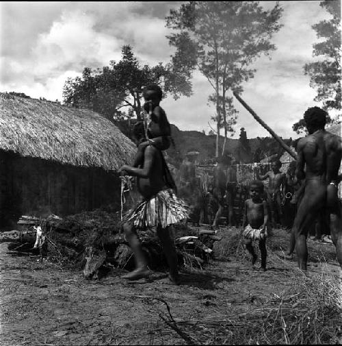 Carrying stones to the haksé; little girl; with child on her shoulders walks past the fire