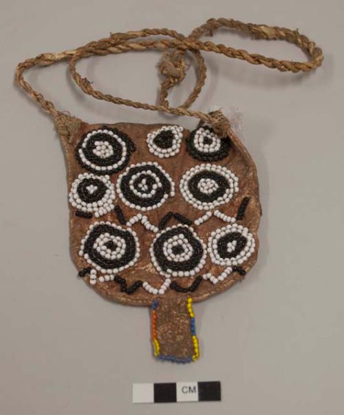 Small leather bag beaded on one side with black and white circular motifs, black and white zigzags; dangling rectangular leather element at base of bag edged with yellow, blue and orange beads; long twisted leather strap