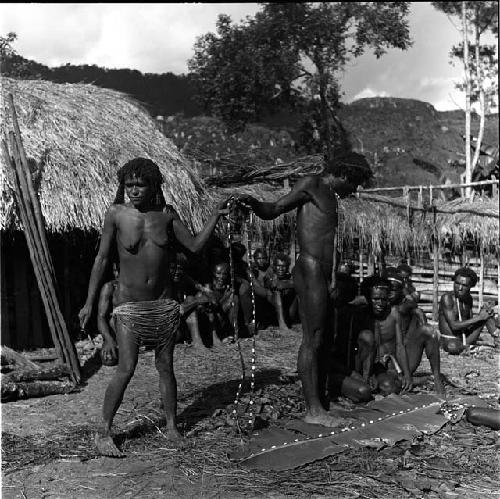 Weaklekek hands a woman a nyeraken aré; others are on the banana leaf in front of him; Asikanilep watches