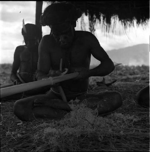 Yegé Asuk whittling his spear