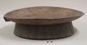 Portable wooden table for serving injera; top unadorned, underneath carved with linear and zigzag designs