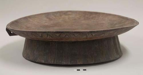 Portable wooden table for serving injera; top unadorned, underneath carved with linear and zigzag designs