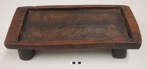 Rectangular serving tray on four legs, carved out of a single piece of wood; top has raised edge. Also used as a chopping block.
