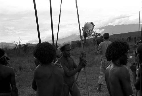 Warriors with spears standing around; researcher and camera in background