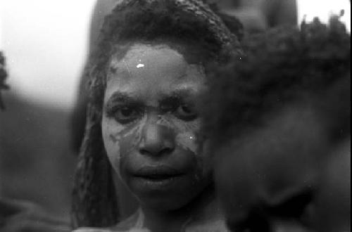 A woman with chalk on her face looks towards the camera