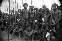 A group of warriors sitting and standing at an Etai -- some look towards camera