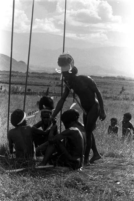 Men greet each other at an Etai; spears around them resting vertically in the ground