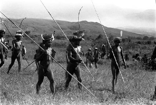 Decorated adult warriors, spears in hand, finding a place to sit down