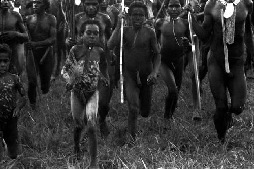 Boys and men dancing, some with spears