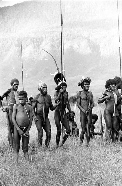 Men watch others dancing at an Etai, some with long spears in hand