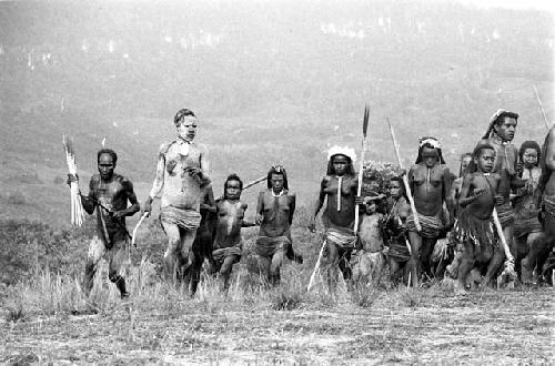 Large group of women dancing, some men among them -- woman on far left covered in clay