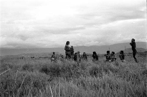 Women's group sitting and standing among the grass at an Etai