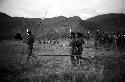 Men dancing, spears in hand -- others dancing in background; hills beyond