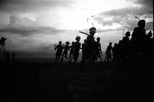 Dancing group of men silhouetted against the low sun; video camera on left of frame