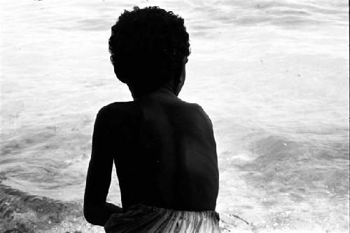 Child with back to camera looks out at water