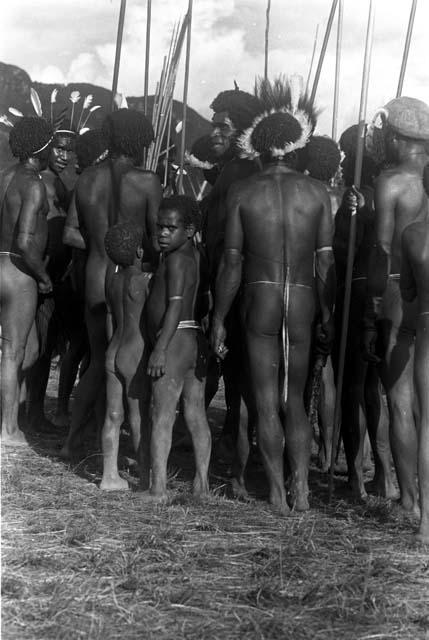 Backs of a men's group at an Etai; one boy turns towards the camera