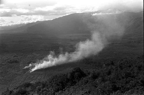 Smoke from a garden below reaches into the air -- seen from high above on a hill