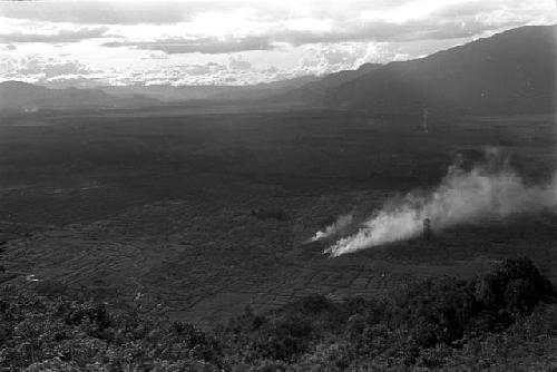 Smoke from a garden below reaches into the air -- seen from high above on a hill; view of surrounding gardens