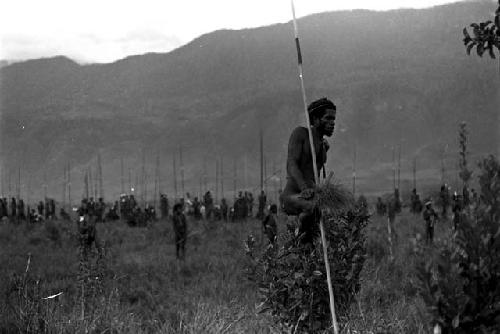 A man watching from the middle rear group, many others beyond him with spears all around