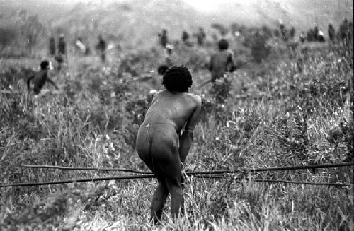 Man with spears crouched in the foreground, action beyond him