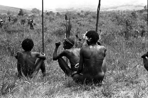 Seated men with weapons, watching the distant action