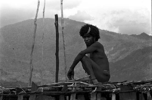 A man seated on the henapu (sleeping platform) of a honai under construction in the new village of Kumina
