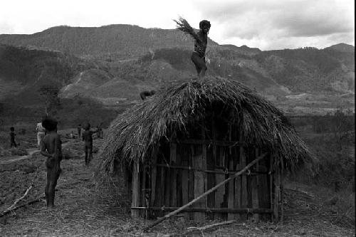 Men thatching the roof of a building under construction in the new village of Kumina; hills beyond