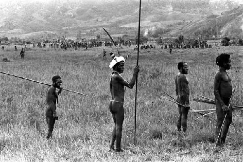 Warriors watch the battle with their weapons in hand; large groups of warriors and hills beyond