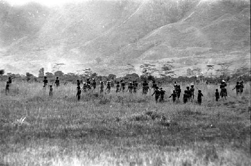 Warriors walking along the Tokolik with weapons in hand; hills beyond