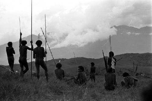 Seated and standing warriors with weapons -- watching the war from a distance