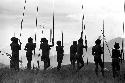 Warriors leaning on their long spears, watching a war in the distance
