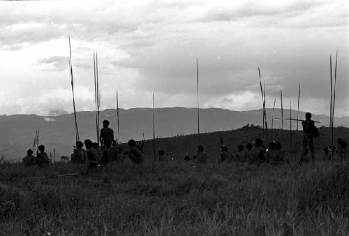 Men waiting with their weapons; Wittaia seen very distant in the middle ground; mountains beyond