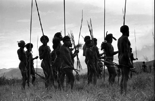 A group of warriors stand with their spears, watching the battle front