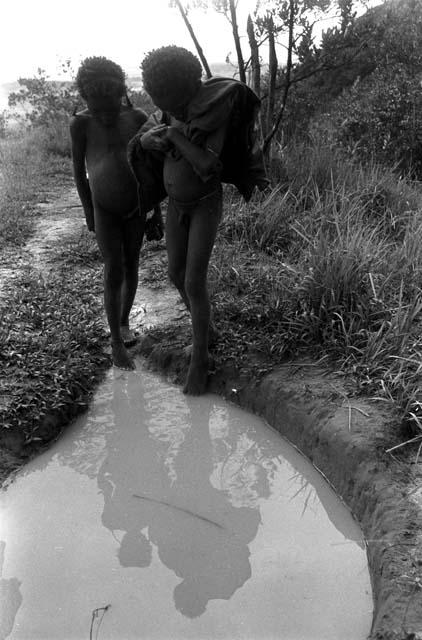 Two young boys look into a puddle