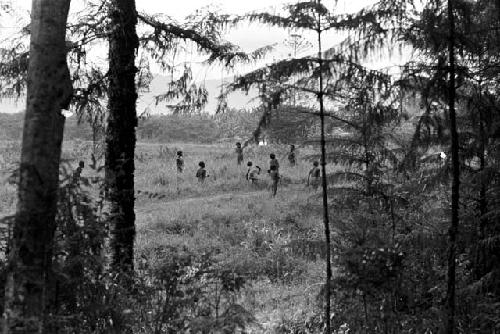 Distant view of men on a field, taken from a wooded area