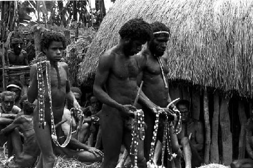 Men bringing the cowrie strings to place around the corpse