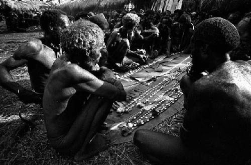 Men looking at cowrie shell strands at Ekiarotmilek's funeral