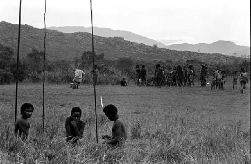 Children with spears in the foreground; Michael Rockefeller in the background near a group of women