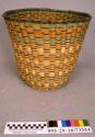 Plaited wicker waste basket with rust, yellow, and green rectangle motif