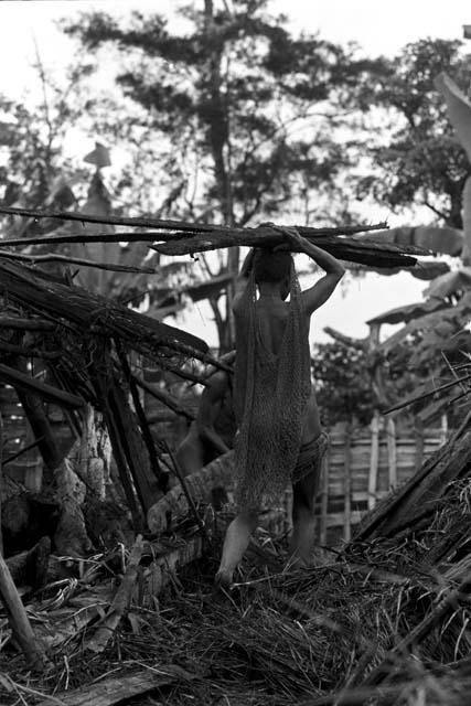 A woman carrying wood on her head while tearing apart an old hunu in Abukulmo