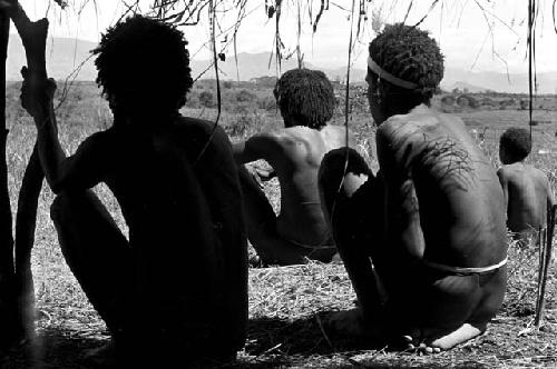 Men seated beneath an oléa waiting for the war to begin