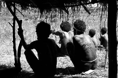 Men seated beneath an oléa waiting for the war to begin