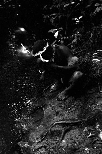 A man crouches by some water