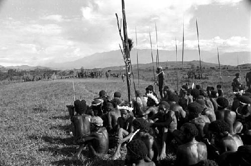 Men seated at an Etai watch dancers beyond them