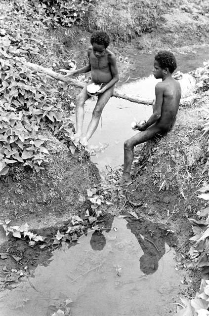 Boys sit by an irrigation ditch