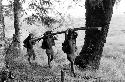 Women carrying large poles past Homoak