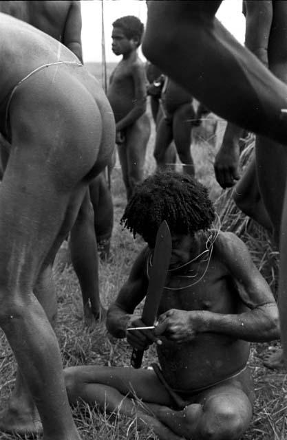 A warrior refines his arrow with a machete