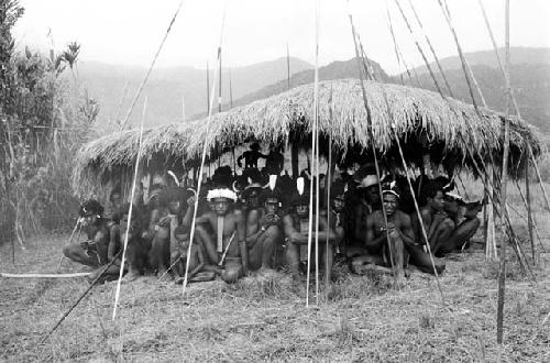 Men sit under an oléa on the Liberek, their spears around them